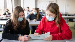 Schülerinnen nehmen mit Mund- und Nasenschutz am Unterricht teil.