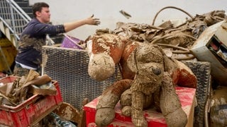 Schlammverschmierte Kuscheltiere liegen auf einem Berg von Sperrmüll