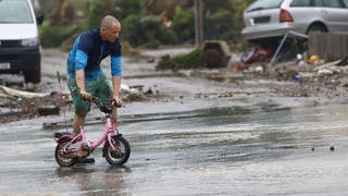 Ein Mann schiebt nach der Flut ein Kinderfahrrad durch den Schlamm.