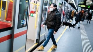 Ein Mann trägt einen Mundschutz und steigt in einen Zug ein