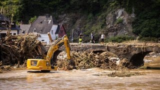 Ein im Fluss Ahr stehender Bagger bei Ahrbrück räumt Schutt aus dem Weg.