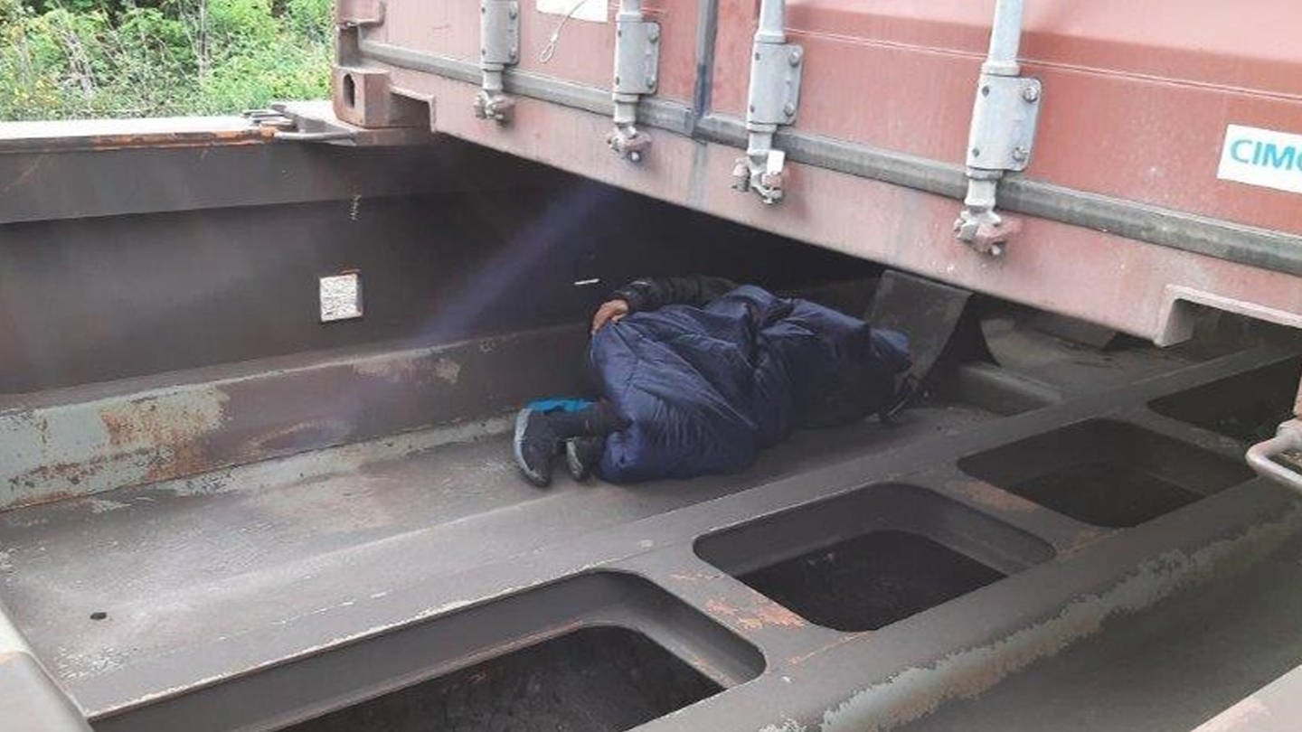 Ein Mann liegt auf dem Auflieger eines Güterwaggons, sein Gesicht ist nicht zu erkennen. Der Waggon ist mit einem Container beladen.