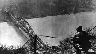 Ein amerikanischer Soldat blickt im Zweiten Weltkrieg auf die Brücke von Remagen (undatiertes Archivfoto). Für US-Amerikaner zählt die Ruine der Rhein-Brücke zwischen Bonn und Koblenz zu den Sehenswürdigkeiten in Deutschland. Denn hier geschah kurz vor Ende des Zweiten Weltkrieges etwas, womit keiner gerechnet hatte.