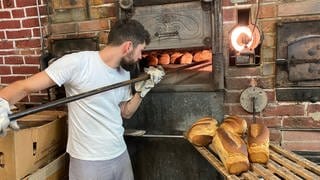 Ein junger Bäcker schiebt Brotlaibe in seinen Holzofen