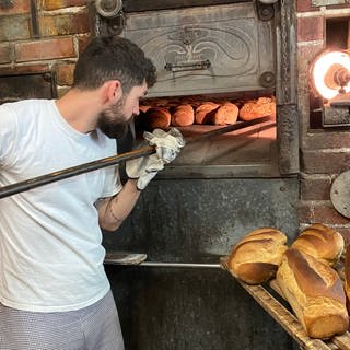 Ein junger Bäcker schiebt Brotlaibe in seinen Holzofen