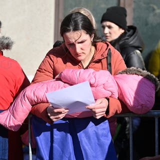 Eine Frau steht in einer Menschenmenge und trägt ihr Kind auf dem Arm