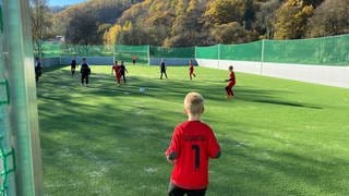 Kinder in roten und schwarzen Trikots spielen auf Fußball-Kleinfeld in Hönningen