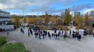 Studenten und Hochschulmitarbeiter stehen auf dem Gelände der Hochschule Koblenz und demonstrieren gegen die geplanten Energiesparmaßnahmen.