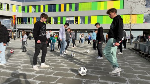 Jugendliche spielen sich gegenseitig Pässe mit einem Ball zu auf einem Schulhof in Bad Marienberg.