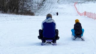Rodel-Spaß bei Kirburg im Westerwald. Vater und Kind von hinten auf Schlitten im Schnee