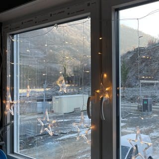Beleuchtete Weihnachtssterne hängen in einem Fenster, aus dem man auf das winterliche Ahrtal blickt 