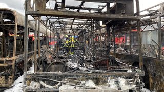 Mehrere Feuerwehrmänner löschen die letzten Brände in einem abgebrannten Bus. Die Feuerwehr schätzt den Sachschaden auf knapp eine Million Euro.