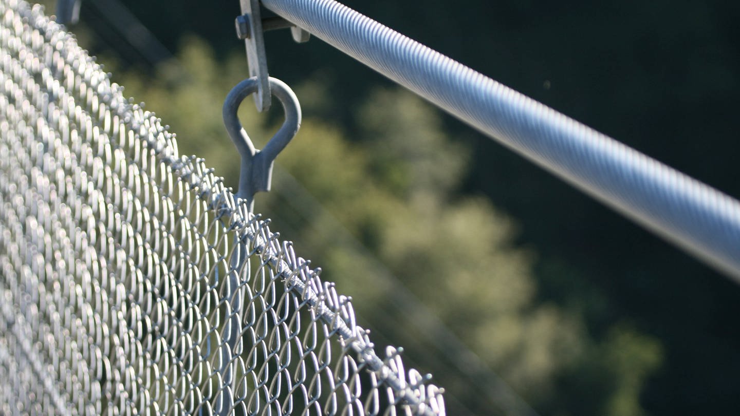 Nahaufnahme eines Gittergeländers aus Metall an einer Hängeseilbrücke
