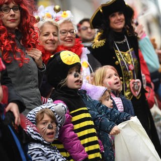 Kinder und Erwachsene stehen verkleidet am Rand eines Karnevalsumzugs.