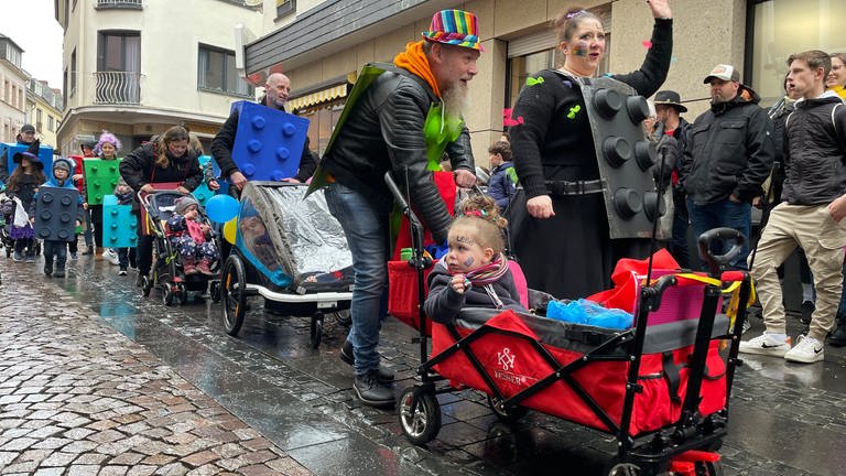 Eltern in Karnevalskostümen schieben die ganz kleinen Kinder im Kinderwagen beim Kinderumzug in Mayen