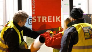 Streikende kleben ein Plakat mit der Aufschrift "Heute Streik" an eine Scheibe. Airport-Mitarbeiter der Luftsicherheit des Flughafens KölnBonn streiken  für bessere Löhne.