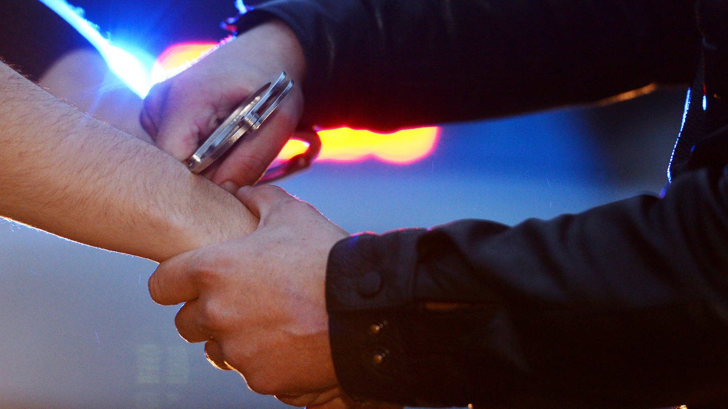 Ein Polizist legt einem jungen Mann Handschellen an