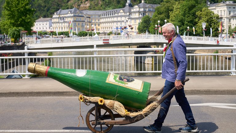Ein Winzer aus Enkirch schiebt beim Festzug des Rheinland-Pfalz-Tages in Bad Ems eine überdimensionale Weinflasche vor sich her.