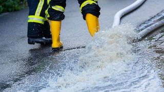 Feuerwehrleute stehen neben einem Schlauch, der Wasser aus einem Keller pumpt