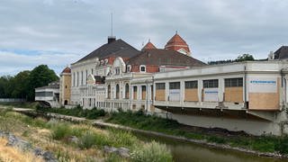 Ein Flussufer mit einem Gebäude. Der Kurpark in Bad Neuenahr-Ahrweiler wurde durch die Wassermassen stark beschädigt. Unter anderem wurde eine Brücke weggerissen. 