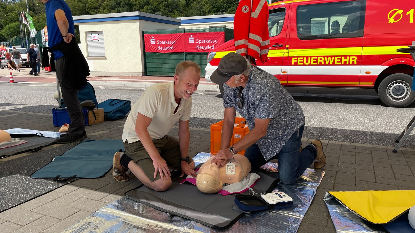 Zwei Besucher üben beim Tue Gutes-Tag in Neustadt Herzdruckmassage an einer Puppe.