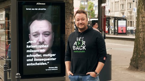 Thomas Pütz vom Helfershuttle steht vor einem Plakat in einer Stadt mit dem bundesweit auf das Ahrtal und seine vergessenen Menschen aufmerksam gemacht werden soll.