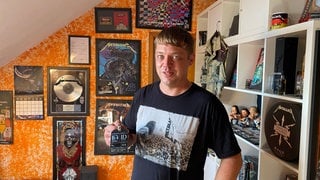 Ein Mann steht in einem Zimmer und hält einen VIP Pass für Metallica in der Hand