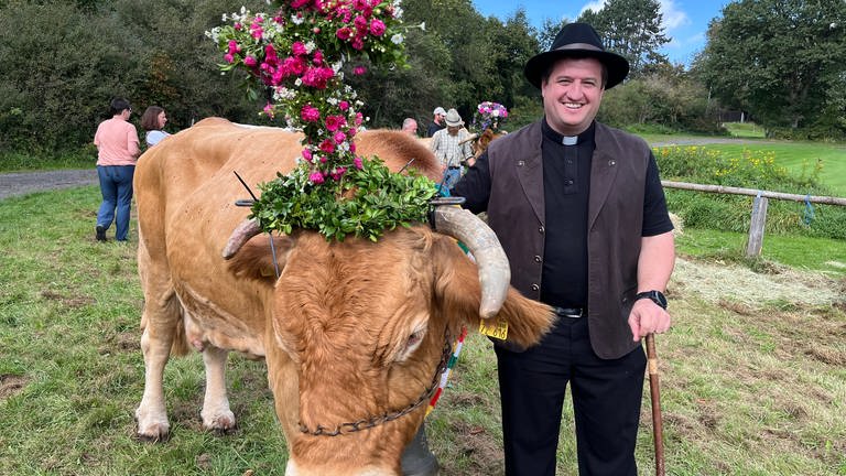 Beim Alm-Abtrieb in Niederelbert im Westerwald hält ein Pfarrer eine Kuh an einem Strick fest.