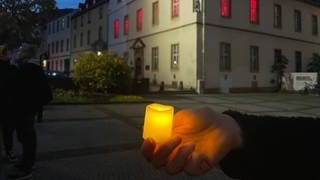 Eine Hand hält eine Kerze vor dem Bürresheimer Hof in Koblenz, der ehemaligen Synagoge. Am 9. November 2023 startete hier der Schweigemarsch zur Erinnerung an 85 Jahre Reichspogromnacht.