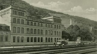 Brauereigebäude mit Biergarten, im Vordergrund Eisenbahngleise, vor der Brauerei Straßenbahnwagen, im Hintergrund rechts Weinberge; um 1930
