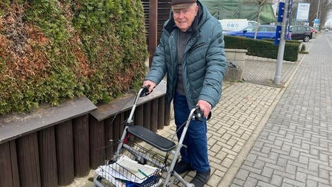Ein älterer Mann steht mit einem Rollator auf einem Bürgersteig