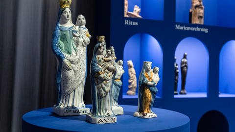 Mehrere Madonnenfiguren auf einem blauen Tisch vor einem blauen Hintergrund: Im Landesmuseum auf der Festung Ehrenbreitstein sind in einer Sonderausstellung jetzt 200 Madonnenfiguren zu sehen