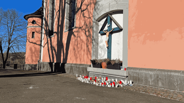 Kerzen stehen vor der katholischen Pfarrkirche in Wissen im Kreis Altenkirchen. Nach der mutmaßlichen Brandstiftung in der Kirche sind die Menschen schockiert und traurig. 
