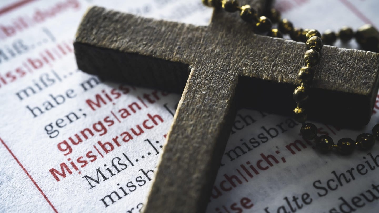 Ein Kreuz auf einem Wörterbuch mit dem Wort Missbrauch: In den 1980er Jahren hatte sich der damalige Pfarrer der katholischen Pfarrei Bassenheim sexuell an einem Kind vergangen. Jetzt sucht das Bistum Trier mögliche weitere Betroffene.