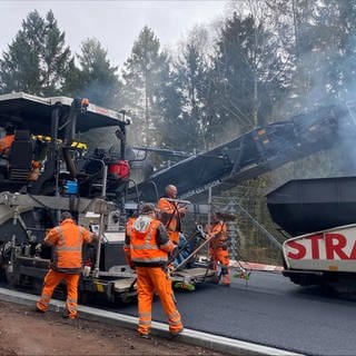 Mehrere große Baustellenfahrzeuge und Bauarbeiter tragen den Asphalt auf der Rennstrecke auf.