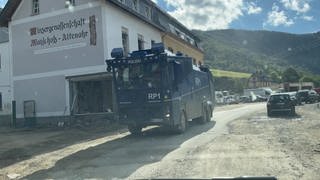 Der Schriftzug "Winzergenossenschaft Mayschoß-Altenahr" an einer Hauswand in Mayschoß, auf der vom Schlamm verstaubten Straße fährt ein Wasserwerferwagen der Polizei