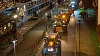 Mehrere Traktoren fahren im Dunkeln am Rhein in Koblenz entlang