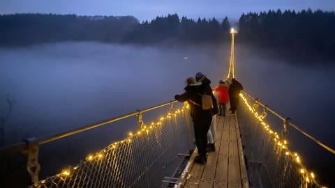 Besucher auf der beleuchteten Geierlay-Brücke im Hunsrück