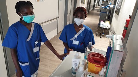 Zwei ausländische Pflegerinnen stehen im Klinikflur an Wagen