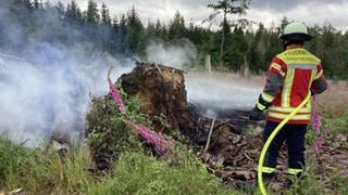 Ein Feuerwehrmann steht mit einem Feuewehrschlauch vor einem Feuer in einem Wald bei Ransbach-Baumbach