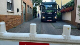 Ein großes Baustellenfahrzeug und zwei Männer, die an einer Straße in Niederlahnstein arbeiten: Unter der Straße hat vermutlich eine Starkstromleitung neben einer Gasleitung gebrannt, die Feuerwehr rückte deshalb zu einem Großeinsatz aus.