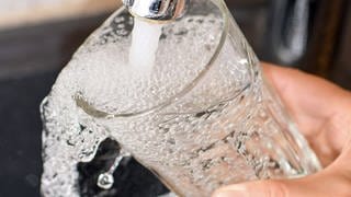 Wasser fließt aus einem Wasserhahn in ein Trinkglas. Sechs Wasserversorger aus dem nördlichen RLP schließen sich zusammen, um sich bei Wasserknappheit gegenseitig zu unterstützen. 