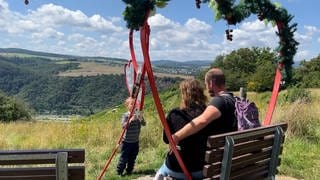 Ein kleiner Junge fotografiert seine Eltern auf einer Themenbank auf dem Wanderweg an der Loreley.