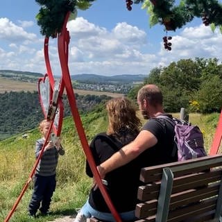 Ein kleiner Junge fotografiert seine Eltern auf einer Themenbank auf dem Wanderweg an der Loreley.