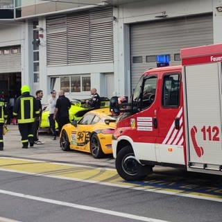 Feuerwehrleute laufen vor Box 27 in der Boxengasse des Nürburgrings. Bei der Explosion einer Druckluftflasche hinter der Box im Bereich des Fahrerlagers wurden etliche Menschen verletzt. 
