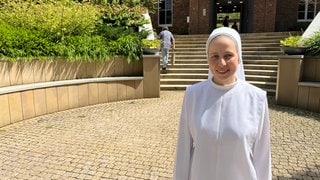 Schwester Clarita steht in ihrem weißen Ordenskleid vor dem Kloster Arenberg in Koblenz.