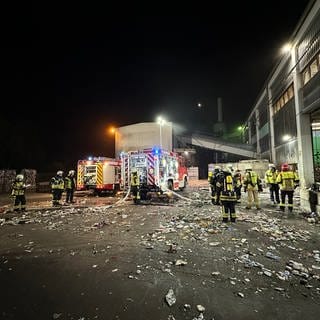 Feuerwehrleute und ein Feuerwehrauto stehen vor der Halle eines Entsorgungsunternehmens