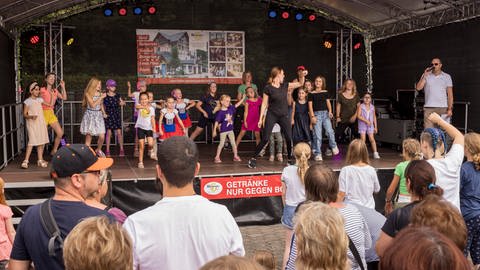 KInder tanzen auf einer Bühne. davor stehen Menschen und schauen zu