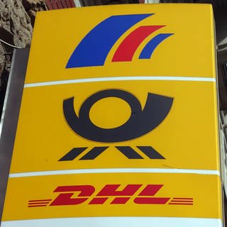 Ein gelbes Hinweisschild auf eine Postbank-, Post- und DHL-Filiale.