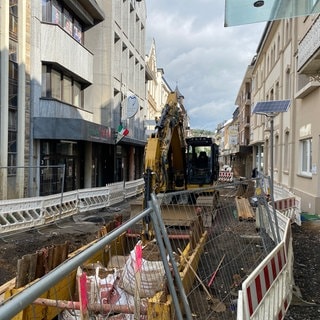 Ein Bagger hat mitten auf der von der Flut zerstörten Poststraße in Bad Neuenahr ein tiefes Loch gebaggert. Schon seit Monaten wird die Straße wieder hergerichtet. Anwohner sind Lärm und Schmutz ausgesetzt.